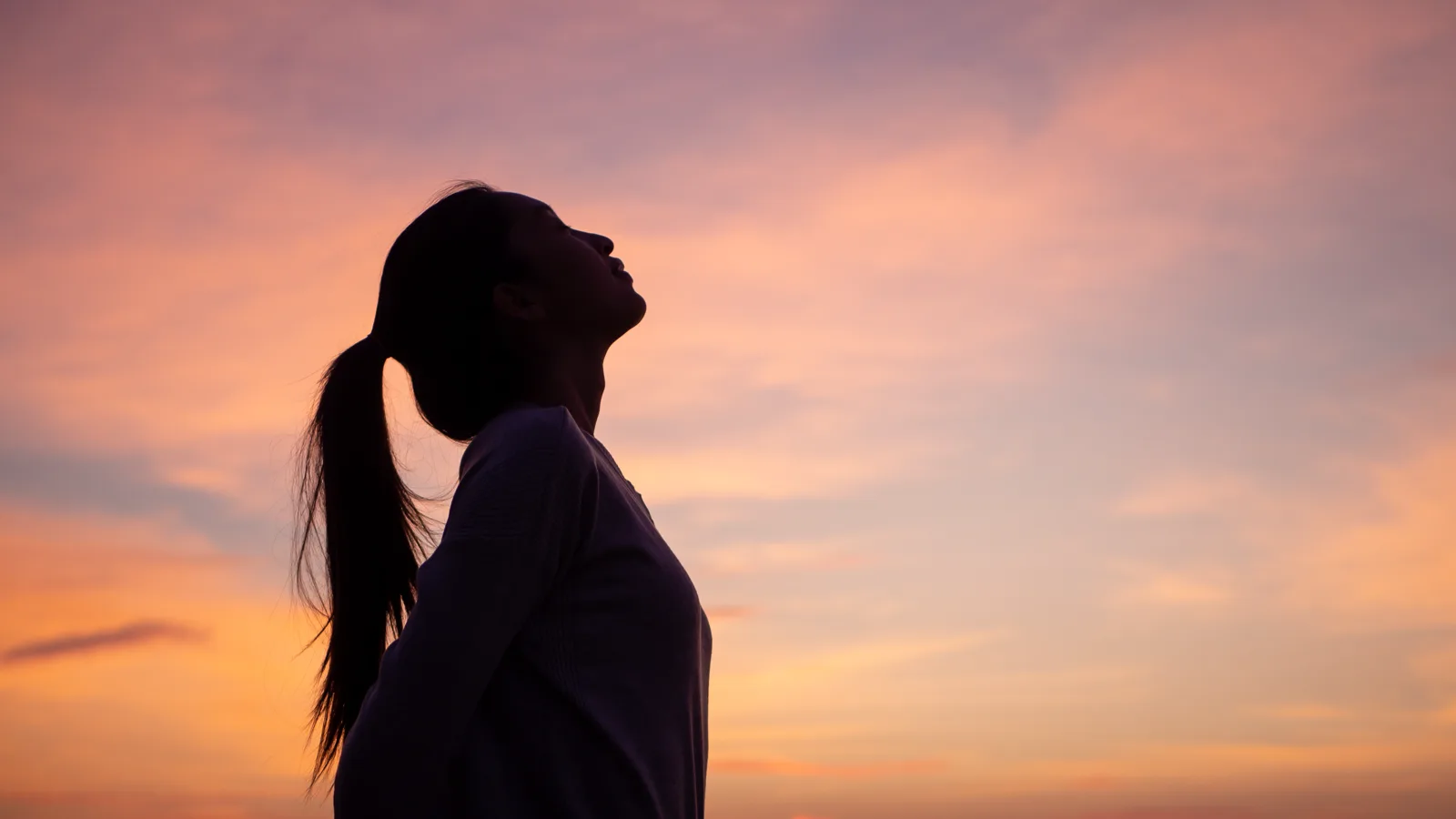Woman silhouetted against a sunset sky, breathing deeply