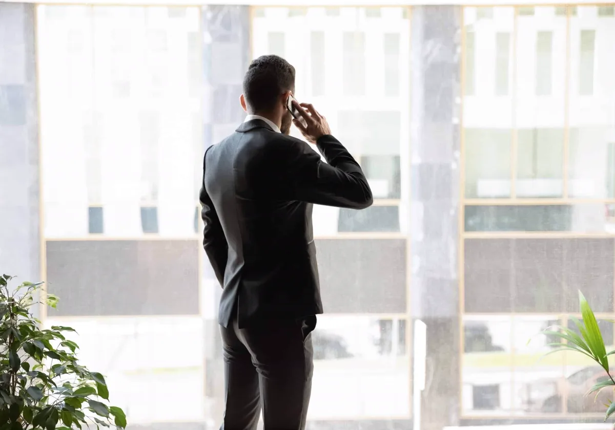 An executive on a phone call at an office window, photographed from behind