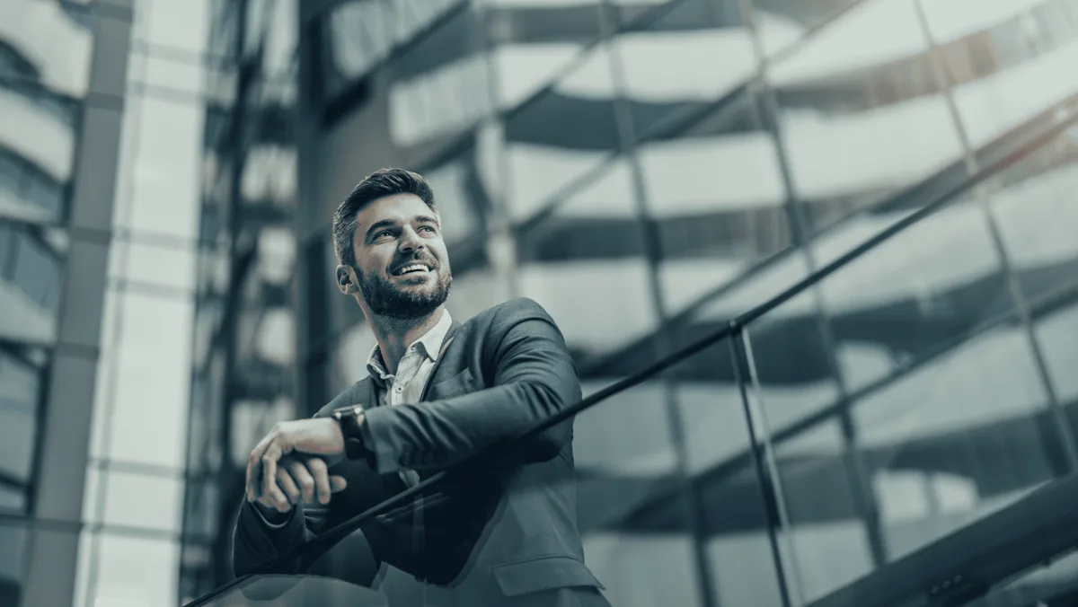 An executive standing at a high office window during the working day, photographed from behind